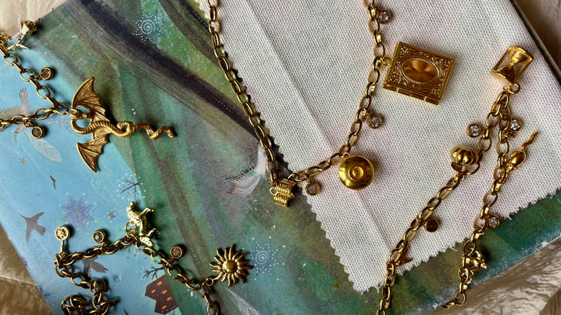 Gold necklaces with various charms on a scenic notebook background